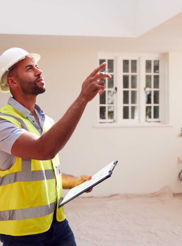 Building Surveyor Wearing Hard Hat With Clipboard Looking At Interior Of New Property